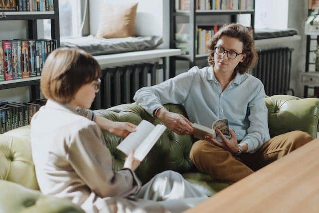 Two individuals discussing their personal goals and motivations while seated in a cozy living room, wit
h one referencing a book.